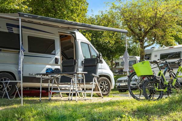 Campingvogn parkeret på campingpladsen med cykler og stole under markisen.