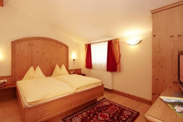 Camera doppia al Sportcamp Woferlgut con letto in legno, cuscini e tappeto decorativo.