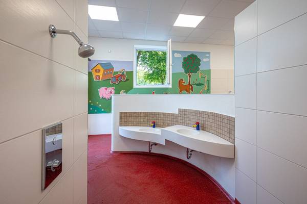 Baño infantil con suelo rojo y pinturas de animales de granja y árboles.