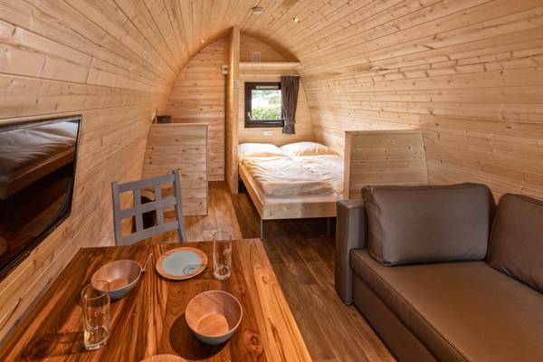 Vista interior de un alojamiento de camping con paredes de madera, una cama, un televisor y una mesa.