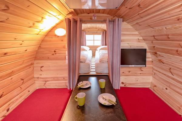Vista interior de una casa de vacaciones de madera con camas, mesa y televisión