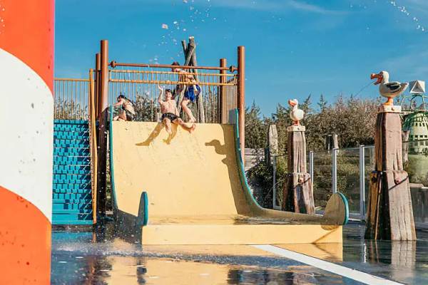 Kinder spielen auf einer Wasserrutsche im Freibad des Campingplatzes Strandpark De Zeeuwse Kust.