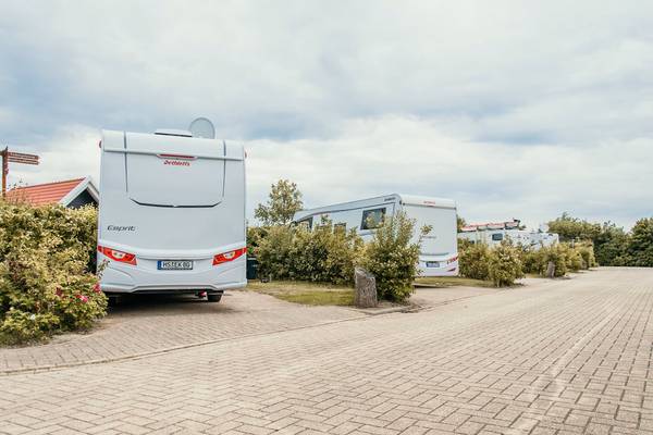 Campingplatz mit Wohnmobilen unter bewölktem Himmel, nahe Büschen.
