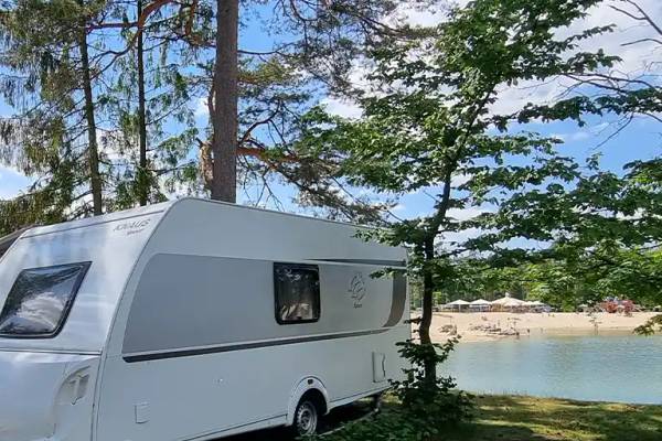 Hvid campingvogn på Südsee-Camp campingplads i et skovområde ved en sø
