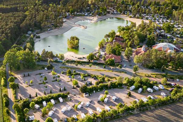 Luftaufnahme vom Sudsee Camp Campingplatz mit einem See und vielen geparkten Wohnmobilen.