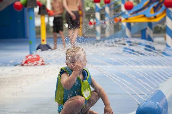 Kind auf Wasserspielplatz im Camping De Paal, bedeckt Gesicht mit Händen