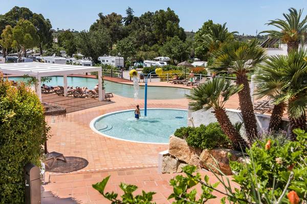 Área de piscina en el Turiscampo Camping Club Algarve con una persona nadando y tumbonas.