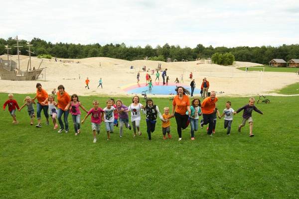 Gruppe von Kindern läuft auf Camping De Paal mit Sandgrube und Spielplatz im Hintergrund.