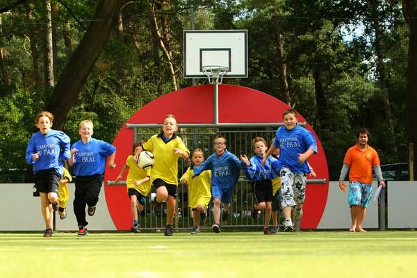 Kinder spielen Fussball auf Camping De Paal, laufen auf ein rotes Tor zu.