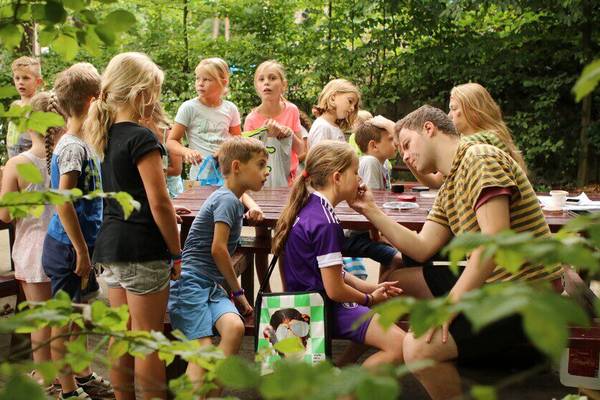 Kinder im Camping De Paal bei einer Freiluftaktivität mit einem Mann, der Gesichtsbemalung anwendet.