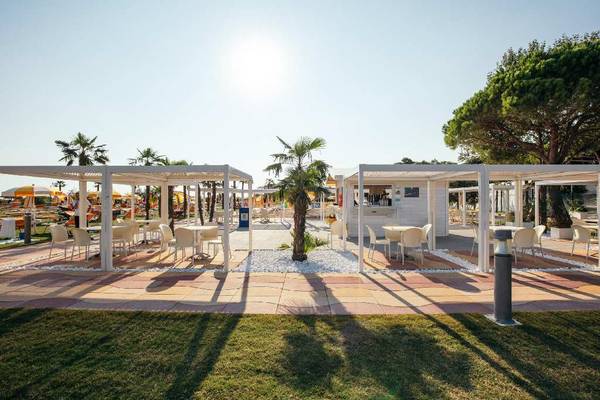 Buiten zitgedeelte op camping Villaggio Turistico Internazionale met witte structuren, tafels en stoelen.