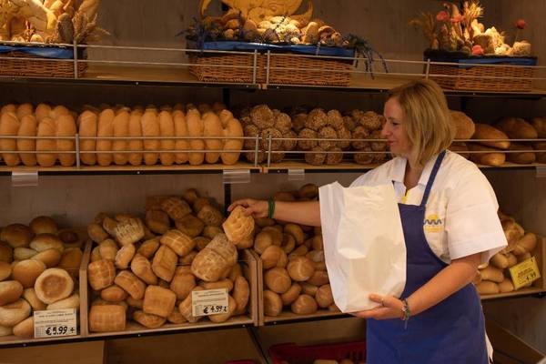 Vrouw in een winkel met een zak brood voor schappen vol verschillende soorten brood.