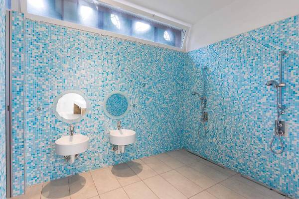 Badkamer met blauwe tegels, twee wastafels en een douche.