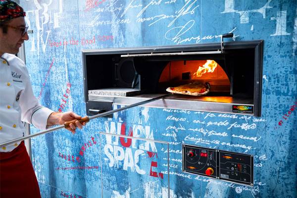 Een chef bakt een pizza in een pizzaoven met vlammen.