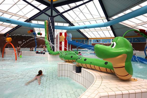 Innenpool im Camping De Paal mit einer großen grünen Rutsche und Wasserspielzeug.