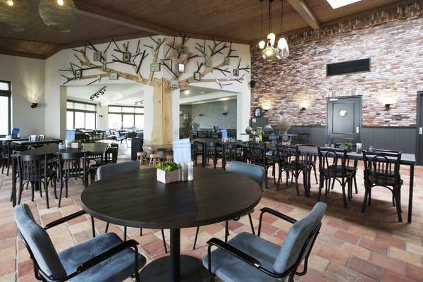 Innenbereich des Restaurants im Camping De Paal mit Holztischen, Ziegelwänden und Baumdesign.