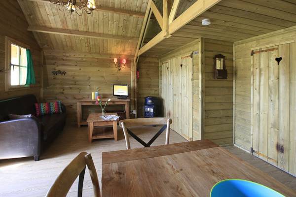 Innenbereich eines Holzchalets im Camping De Paal mit Couch, Tisch und Fernseher.