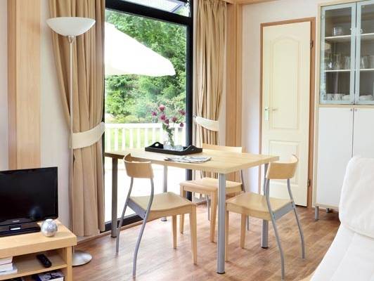 Woonkamer in Camping De Wildhoeve met tafel, stoelen, tv en open raam.