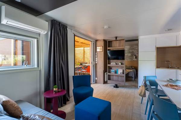 Vue intérieure d'un gîte au Camping Village Le Brasilia avec canapé, table à manger et porte ouverte.