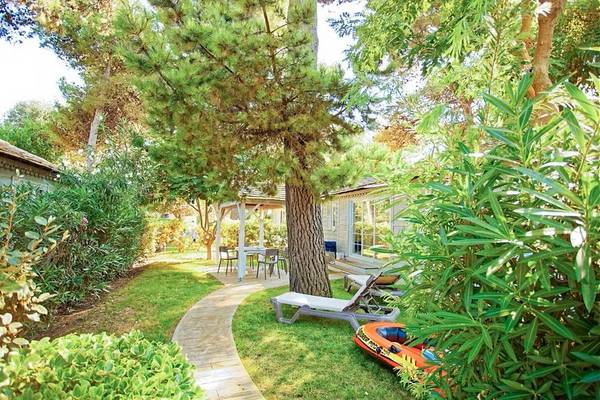 Espace extérieur du Camping Village Le Brasilia avec une maison, une terrasse, des chaises et des arbres.