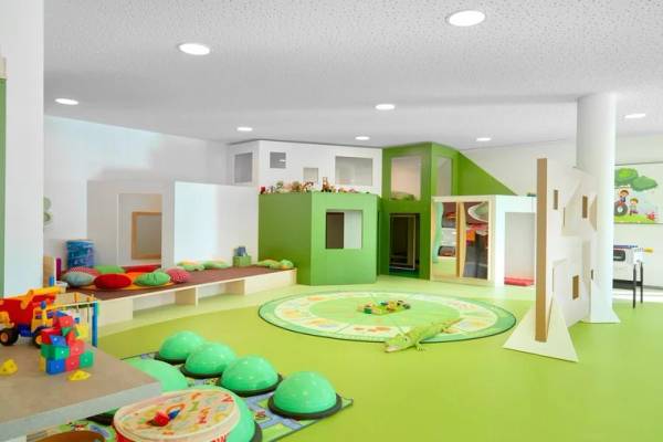 Kinderspielzimmer im Zugspitz Resort mit grünen Wänden, Spielzeug und einer Spielmatte.