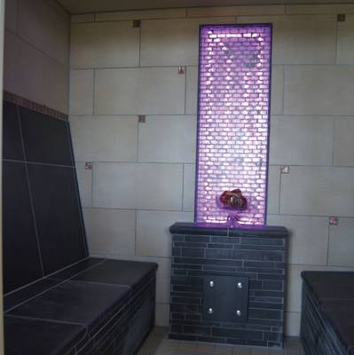 LuxOase Freizeitpark Sauna-Innenraum mit gefliesten Wänden und einer lila Ziegelwand.