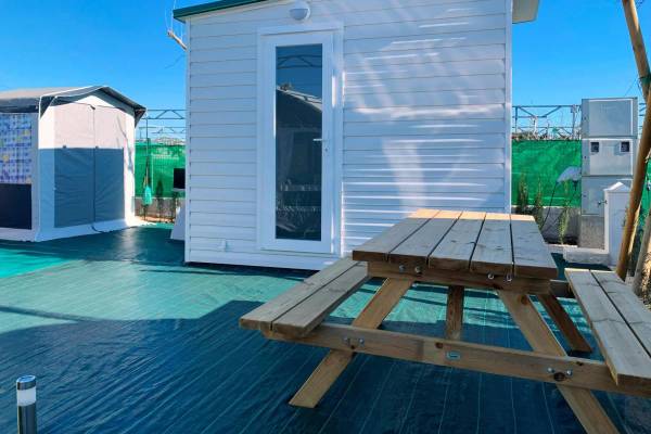 Un camping avec une table de pique-nique en bois et une petite maison devant un ciel bleu clair.