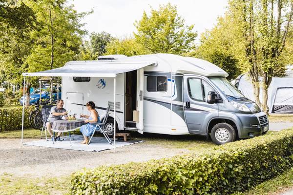 Ein Paar sitzt an einem Tisch unter einem Vordach vor ihrem Wohnmobil.