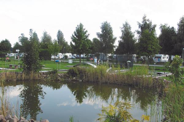 LuxOase Freizeitpark Campingplatz mit Teich und Campingwagen im Hintergrund.