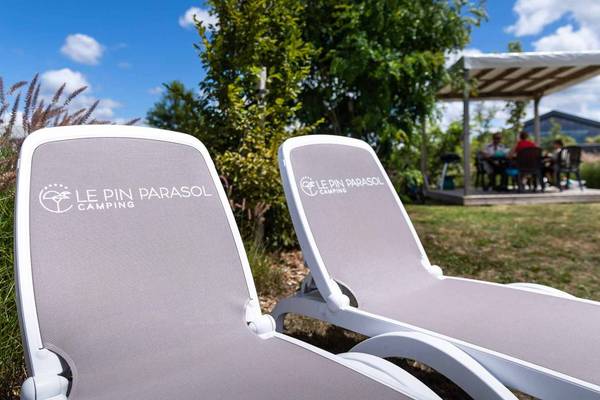 Deux chaises longues au Camping Le Pin Parasol avec un gazebo et des personnes assises en arrière-plan.