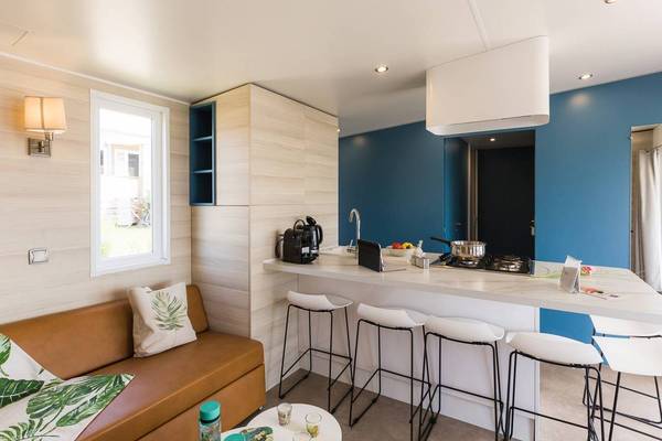 Intérieur du Camping Le Pin Parasol montrant une cuisine moderne avec une cuisinière, un évier et des tabourets.