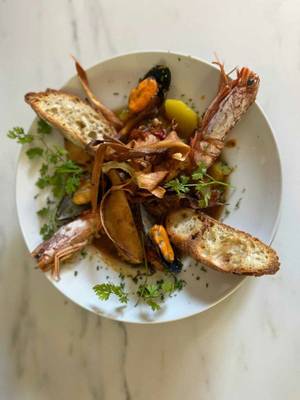 Ein Teller mit Garnelen, Muscheln, Brot und Kräutern auf einer Marmoroberfläche.
