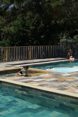 Zwei Schwimmer im Pool des Camping Les Criques de Porteils, einer sitzt am Rand.
