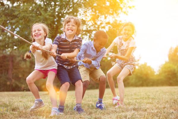 Vier Kinder ziehen gemeinsam an einem Seil in einem Feld auf dem Campingplatz Barco Reale.