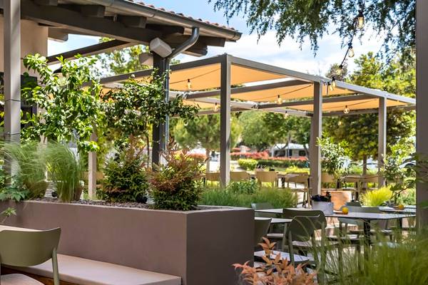 Terrasse au Camping Vestar avec des tables et des chaises entourées de verdure.