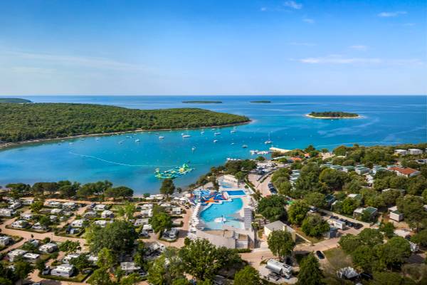 Vue aérienne du Camping Vestar avec une piscine, la mer et de nombreux bateaux au loin.