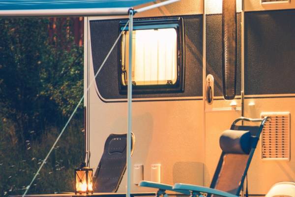 Camping-RV met terras in de avond, verlicht door warm licht, met stoelen en een lantaarn.