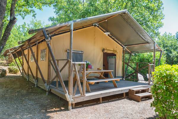 Ein Campingzelt mit Holzplattform, Picknicktisch und Baum im Hintergrund.