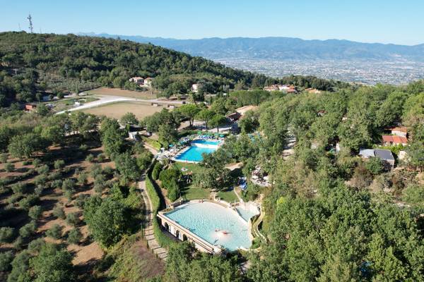 Luftaufnahme eines Campingplatzes mit Schwimmbad, umgeben von Bäumen und Bergen.