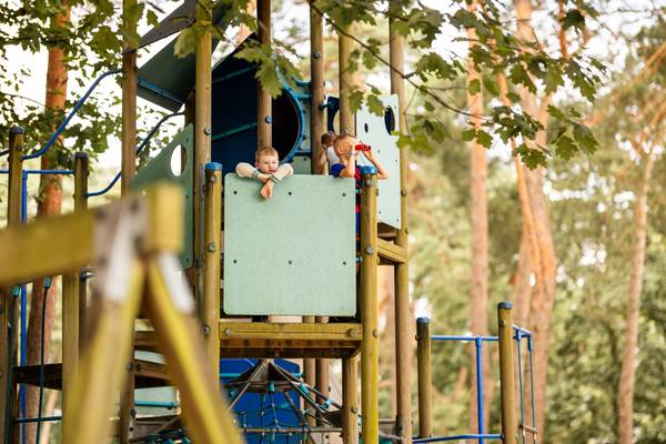 Zwei Kinder schauen aus einem Spielhaus auf einem Spielplatz im Camping De Paal.