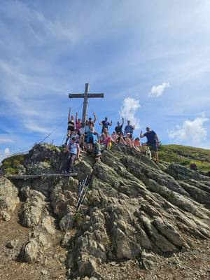 Gruppo di escursionisti sulla cima di una montagna con una croce dietro di loro