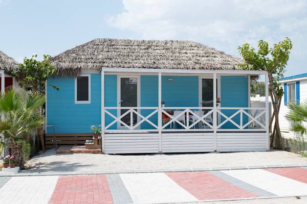 Maison de vacances bleue avec un toit en paille entourée d'autres maisons et de plantes.