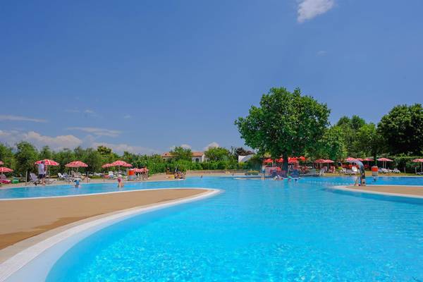 Udend swimmingpool på Fornella Camping & Wellness Family Resort med mennesker, der svømmer og slapper af under den blå himmel.