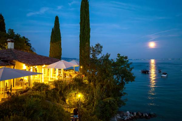 Vista serale del Fornella Camping & Wellness Family Resort con una luna piena riflessa sull'acqua.