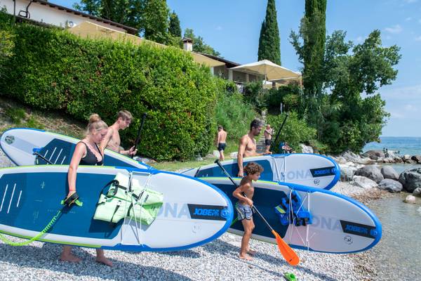 Gruppe af mennesker på Fornella Camping & Wellness Family Resort, der bærer paddleboards til vandet.