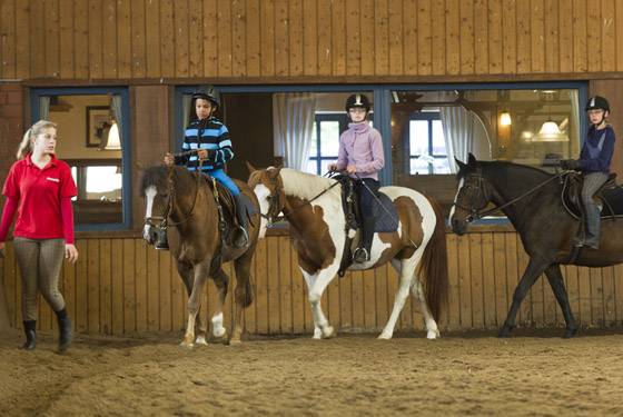 Fire personer rider heste i en stal på Sudsee-Camp.