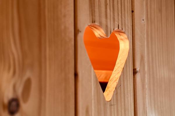 Herzförmige Aussparung in einer Holzwand mit warmem Licht dahinter.