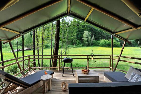 Terrasse eines Campingplatzes im Ferienparadies Natterer See mit Holzloungesesseln, einem Tisch und einem Grill.