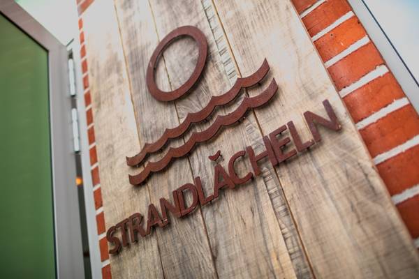 Cartel de madera con el texto 'Strandlächeln' en el camping Insel-Camp Fehmarn.