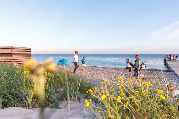 Escena de playa del camping Insel-Camp Fehmarn con personas caminando y una tienda azul